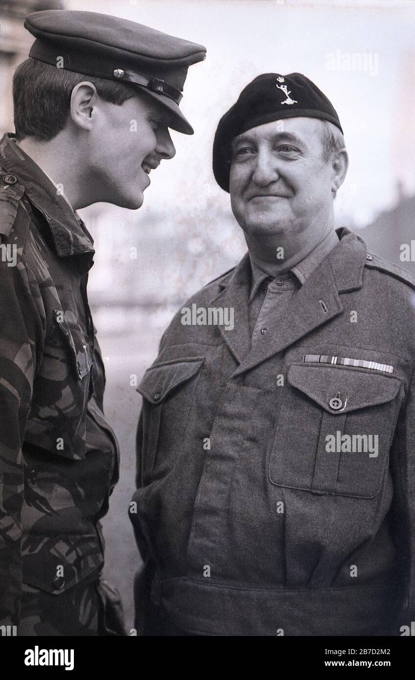Años 80, histórico, un joven oficial del ejército vestido militar moderno,  hablando de cerca de un soldado más viejo, usando uniforme militar  tradicional de los años 40, Inglaterra, Reino Unido. Posiblemente actores