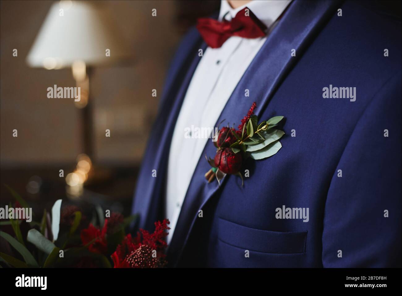 Poner Perforar contraste Elegante novio en traje azul con pajarita roja y boutonniere verde-rojo en  su chaqueta - detalles de la boda Fotografía de stock - Alamy