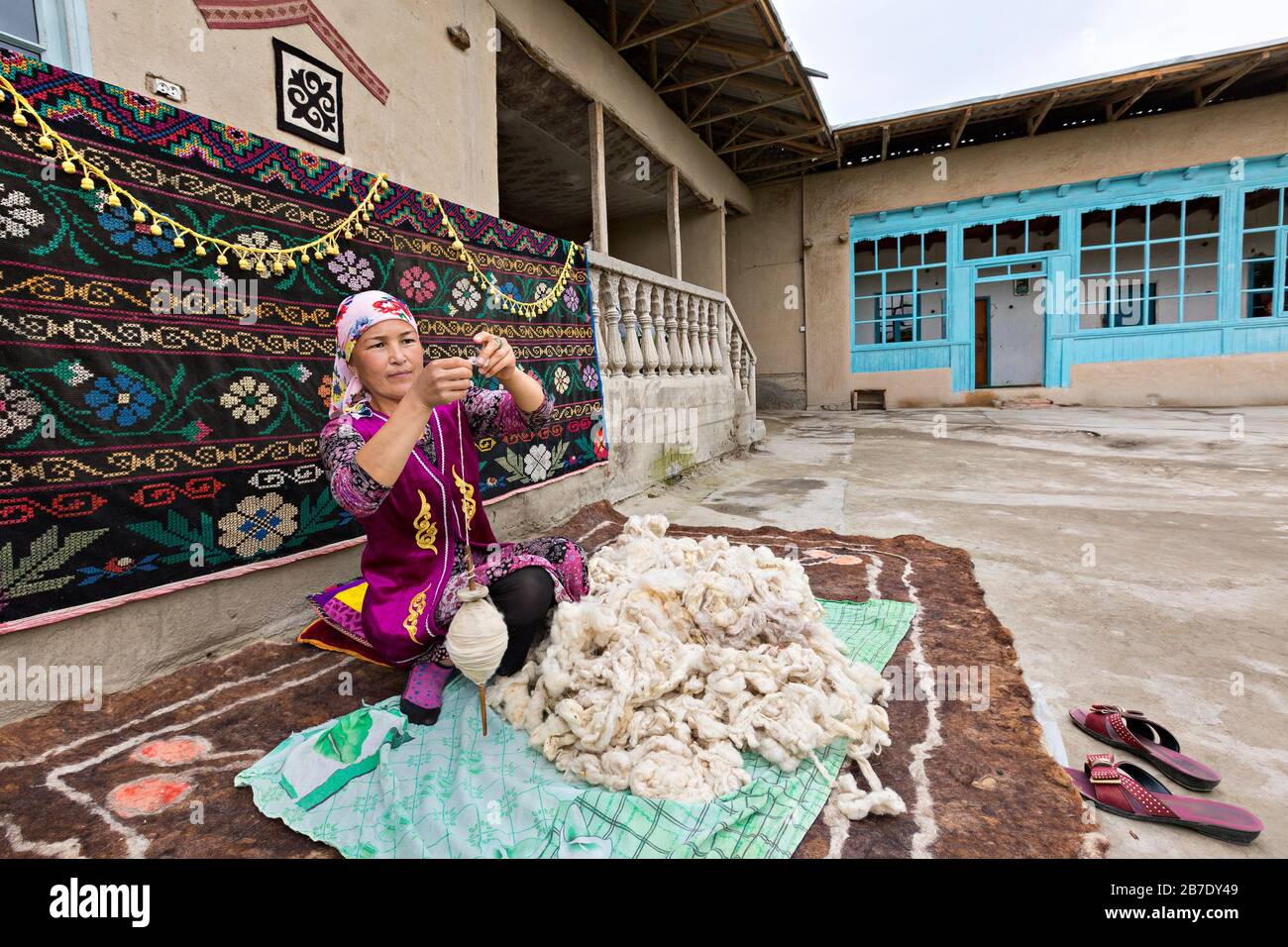 Mujer uzbeka con ropa local que hace girar la lana a mano, en Rishtan, Uzbekistán. Foto de stock