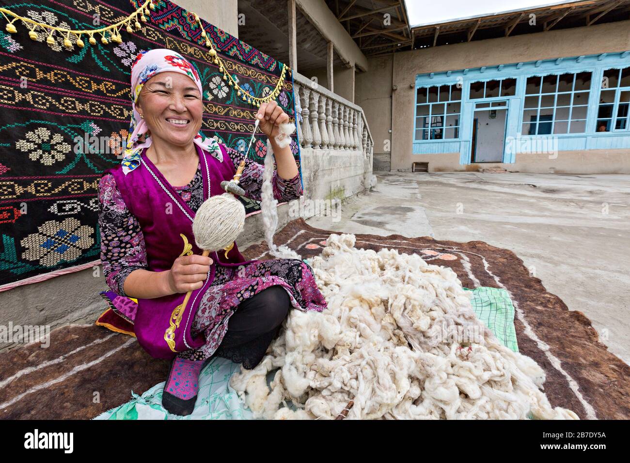 Mujer uzbeka con ropa local que hace girar la lana a mano, en Rishtan, Uzbekistán. Foto de stock