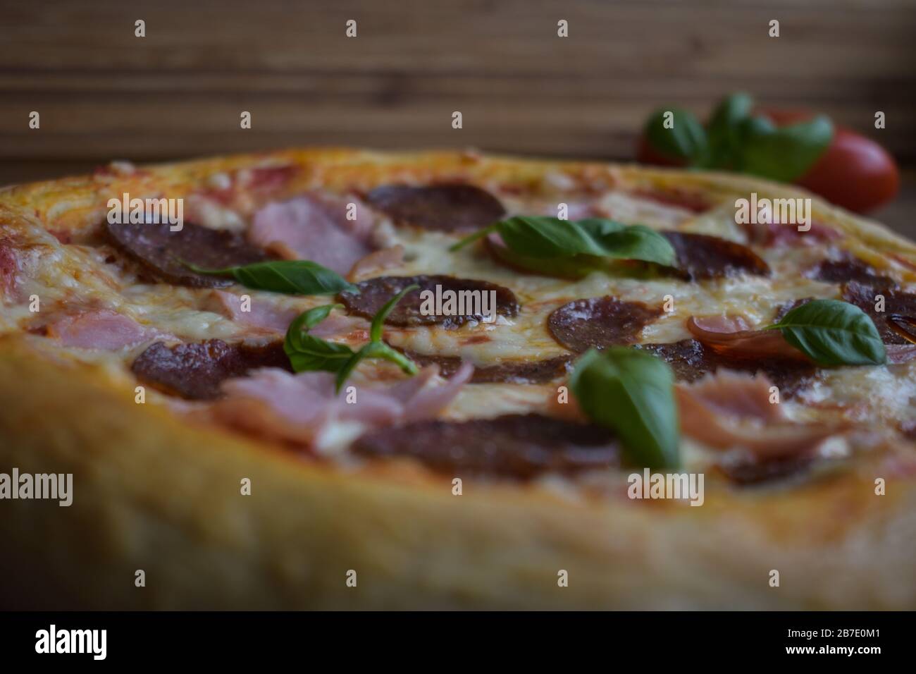 pizza casera al horno sobre piedra de pizza, con peperoni y jamón, adornada  con albahaca Fotografía de stock - Alamy