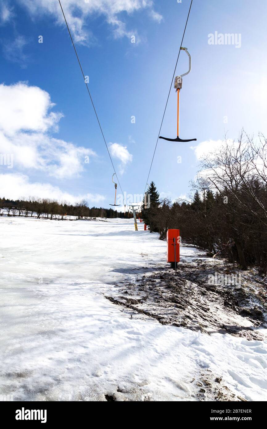 Elevador de superficie de barra en T detenido en pistas vacías, concepto de fin de temporada de esquí, pendiente con nieve desaparecida, invierno soleado o día de primavera Foto de stock