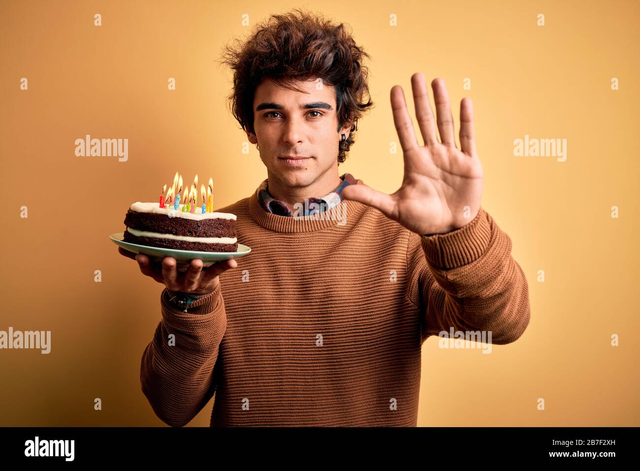 Joven hombre guapo sosteniendo pastel de cumpleaños sobre fondo amarillo  aislado con mano abierta haciendo stop con expresión seria y segura  Fotografía de stock - Alamy
