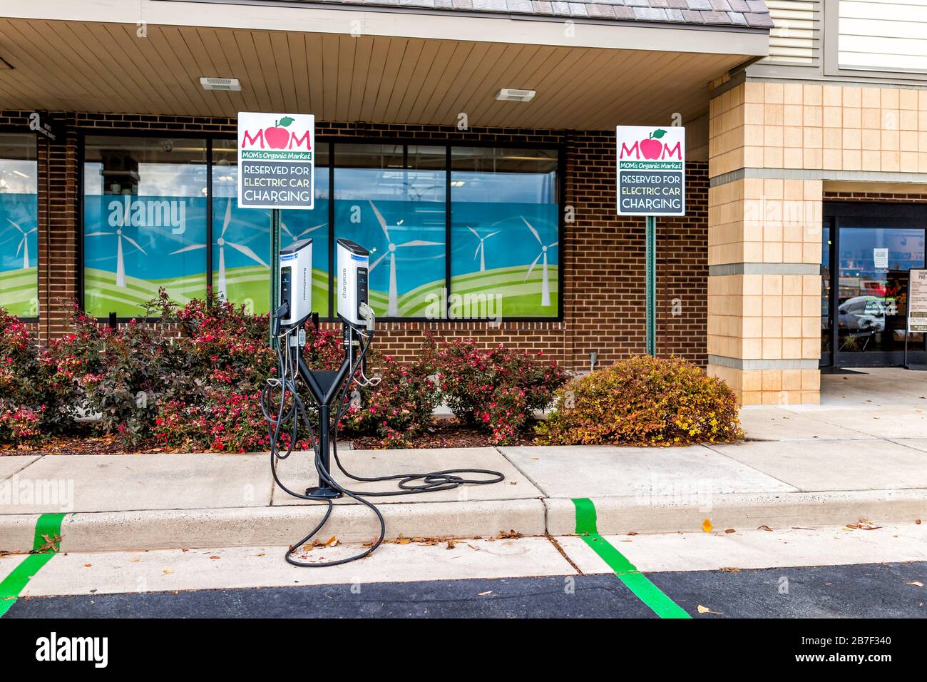 Herndon, EE.UU. - 12 de noviembre de 2019: Estacionamiento de fachada exterior y carga de coche eléctrico de la tienda Mom's Organic Market con productos frescos de granja en el plato Foto de stock
