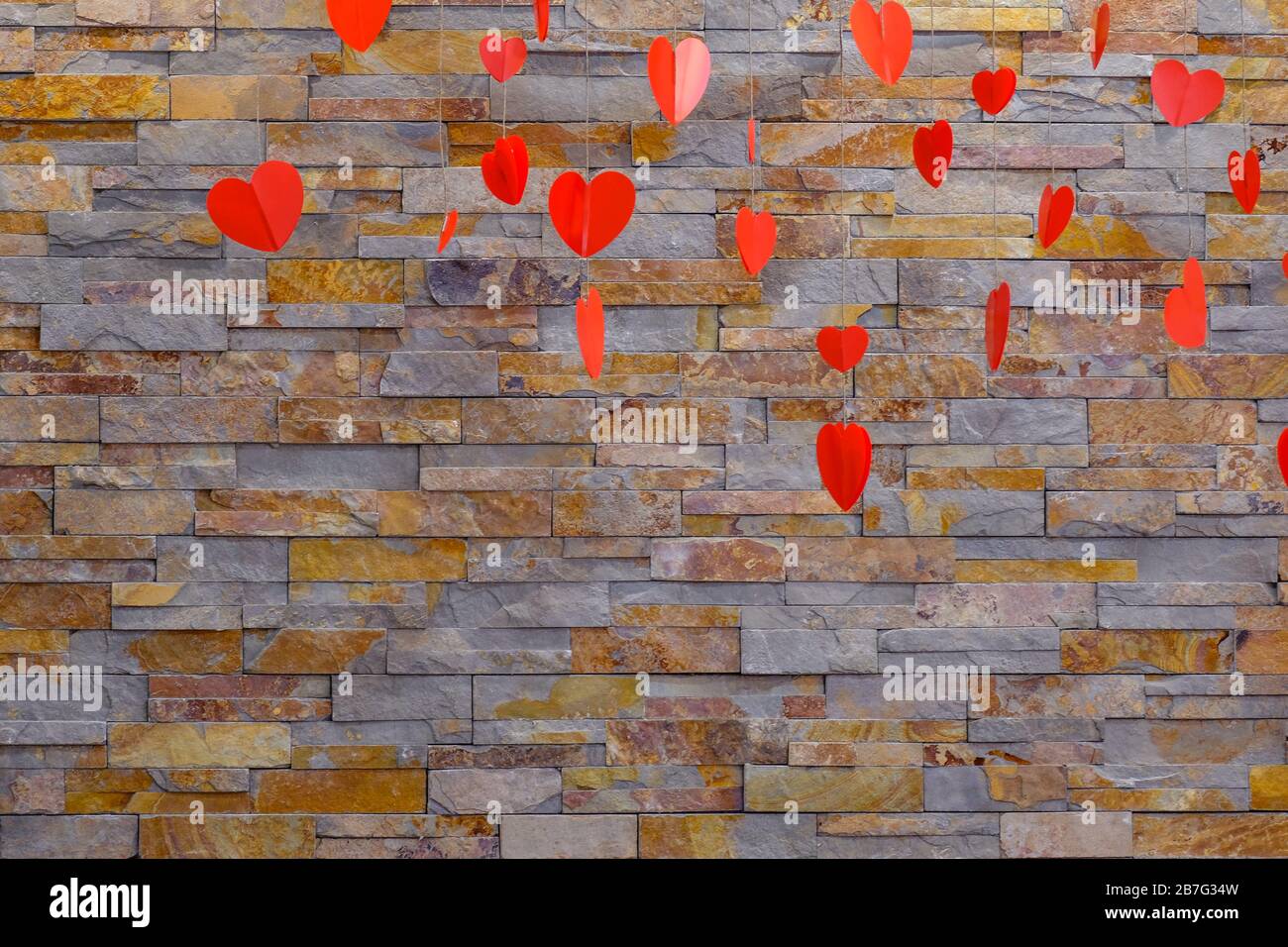 Fondo de piedra artificial en la pared. Colgando corazones rojos para el día de San Valentín. Productos de papel caseros. Foto de stock