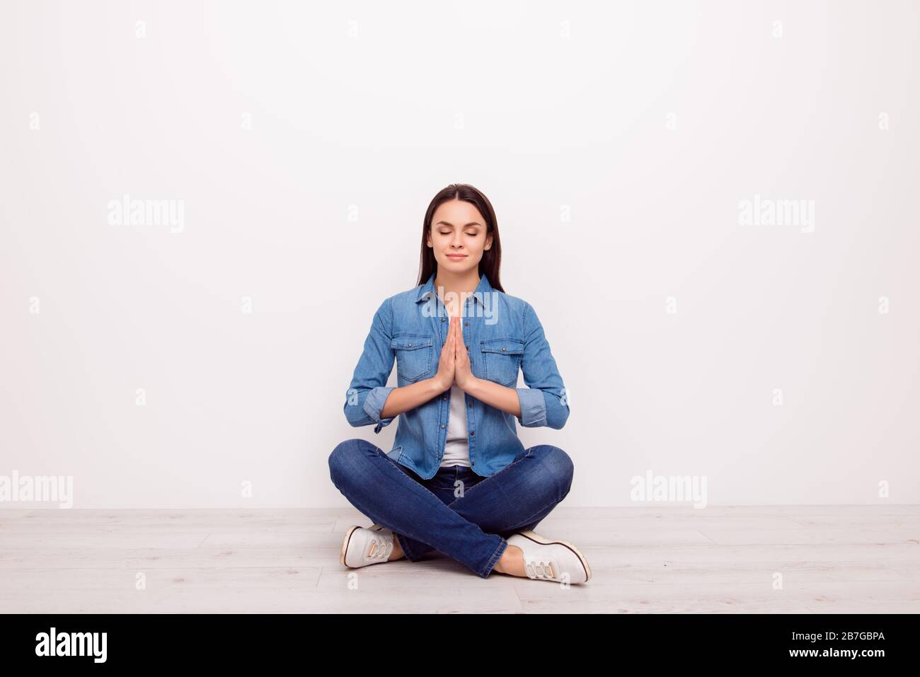 Tranquila relajada bonita chica en jeans sport ropa con las manos, los ojos  cerrados, sentado en una postura de yoga con piernas cruzadas en el suelo  blanco Fotografía de stock - Alamy