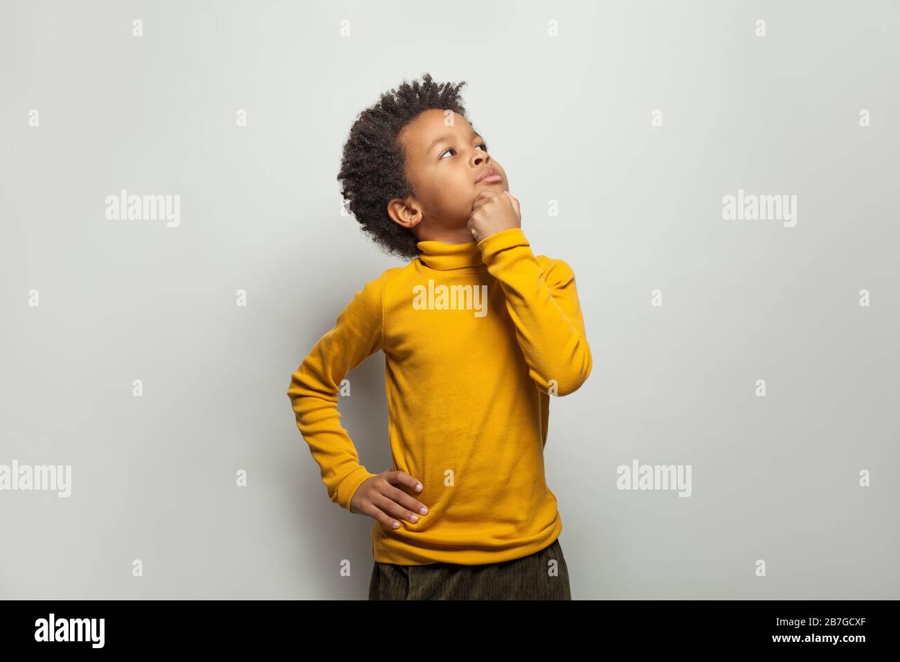 Niño negro curioso mirando hacia arriba sobre fondo blanco Foto de stock