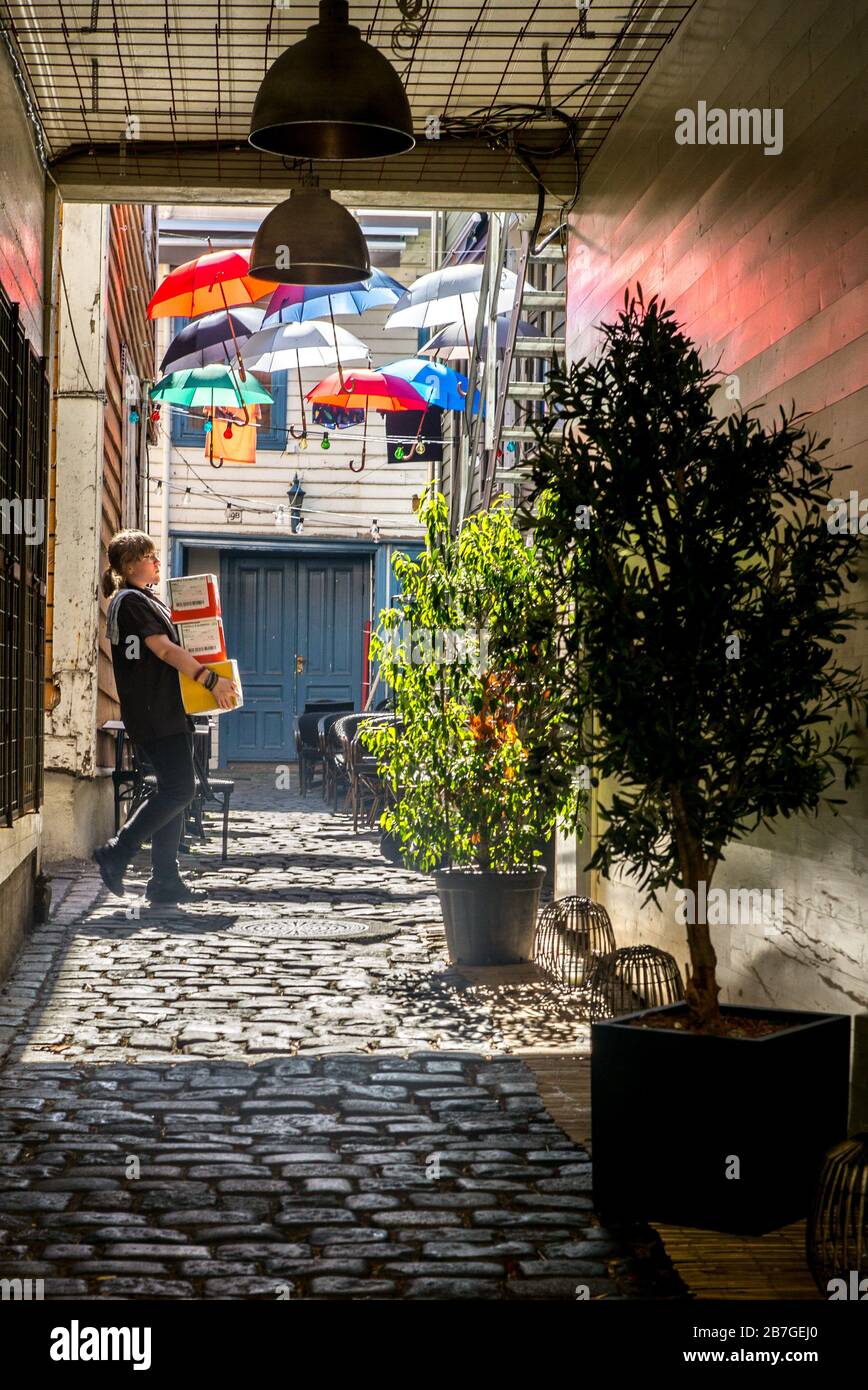 Chica llevando suministros a su café en el patio trasero de Bergen. Paraguas de colores. Foto de stock