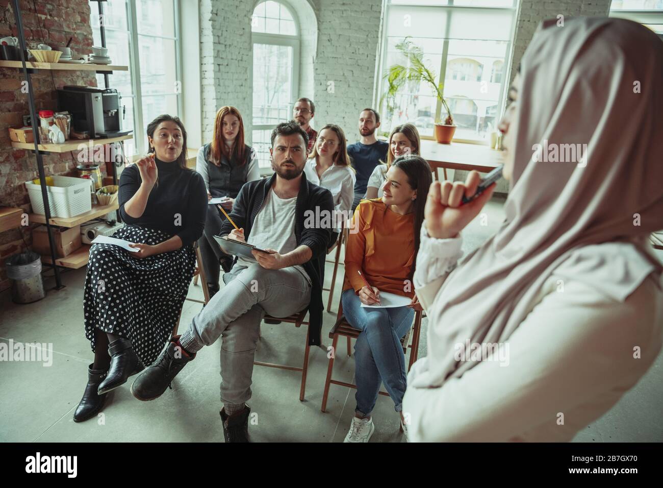 Una oradora musulmana que da una presentación en el salón del taller. Audiencia o sala de conferencias. Preguntar a los participantes en la audiencia. Evento de conferencia, formación. Educación, diversidad, concepto inclusivo. Foto de stock