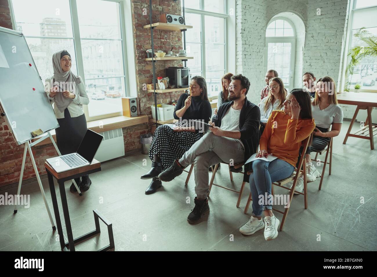 Una oradora musulmana que da una presentación en el salón del taller. Audiencia o sala de conferencias. Riendo a los participantes en el público. Evento de conferencia, formación. Educación, diversidad, concepto inclusivo. Foto de stock