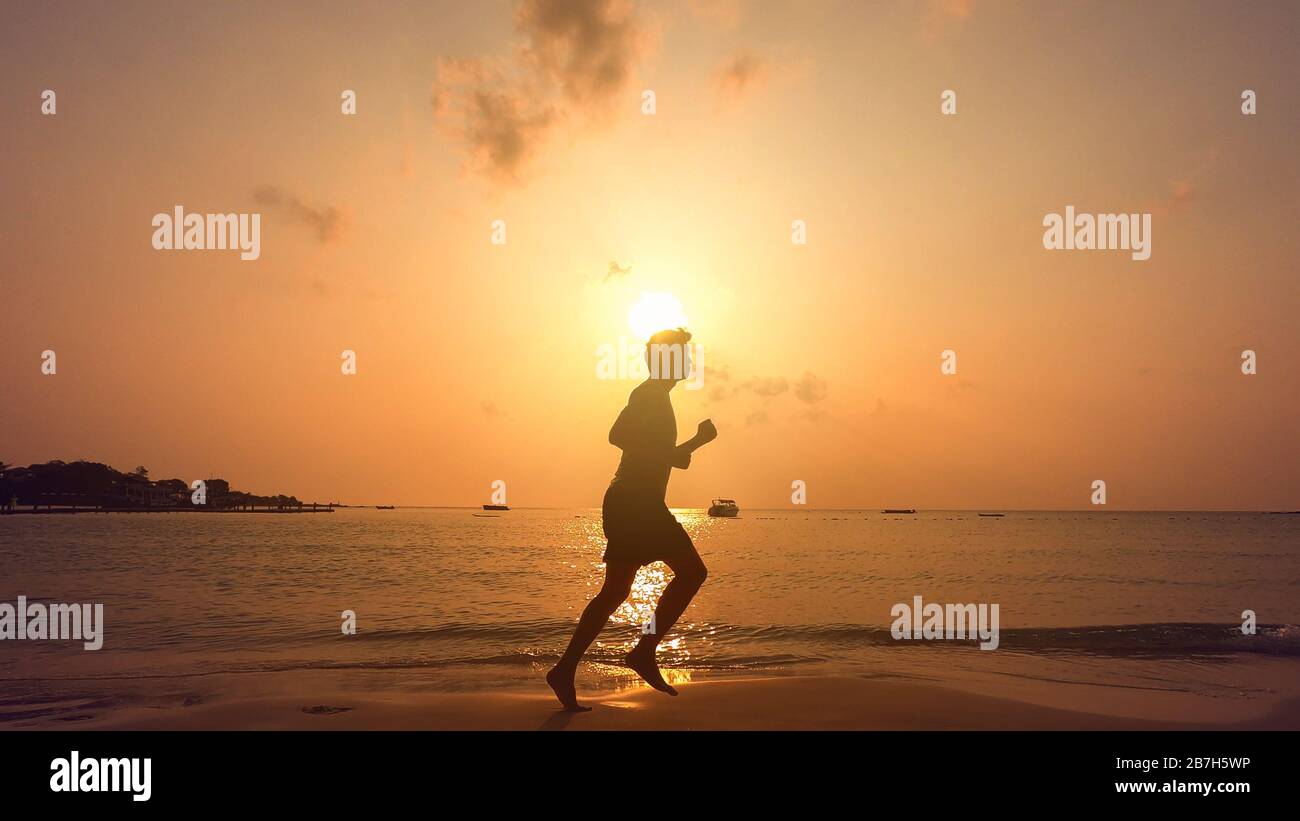 Un hombre descalzo corriendo en la playa al atardecer. Foto de stock