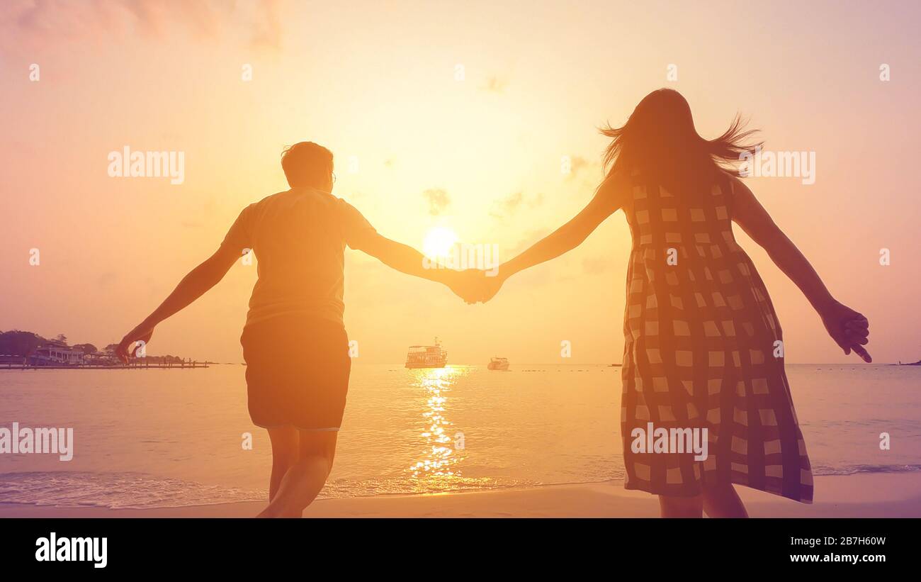 Feliz pareja con las manos caminando hacia el mar Foto de stock