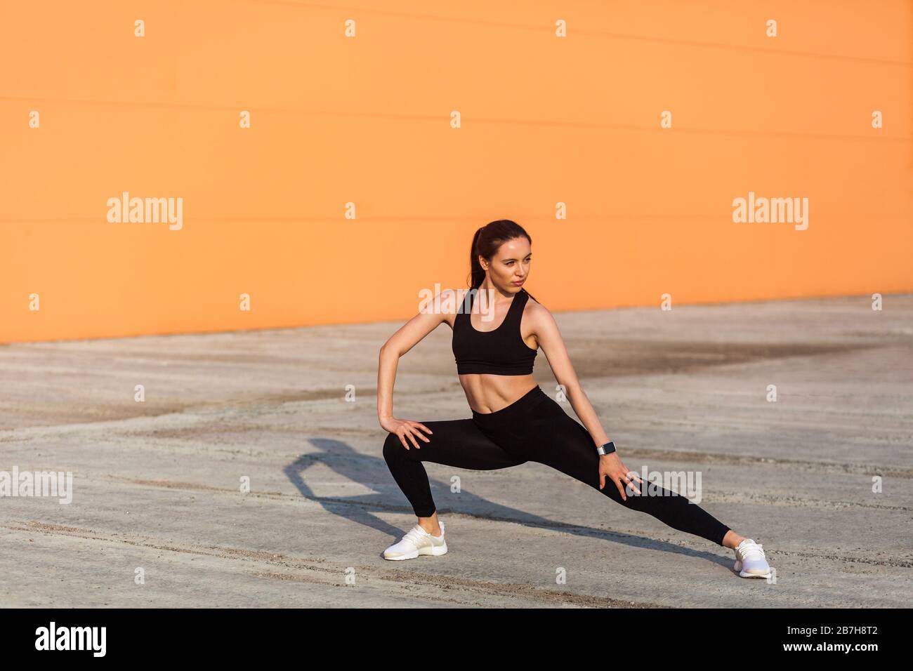 Mujer joven bonita delgada en ropa deportiva ajustada, pantalones negros y  top, practicando al aire libre, haciendo ejercicios de estiramiento para  una mejor flexibilidad, exe de cuerpo inferior Fotografía de stock -