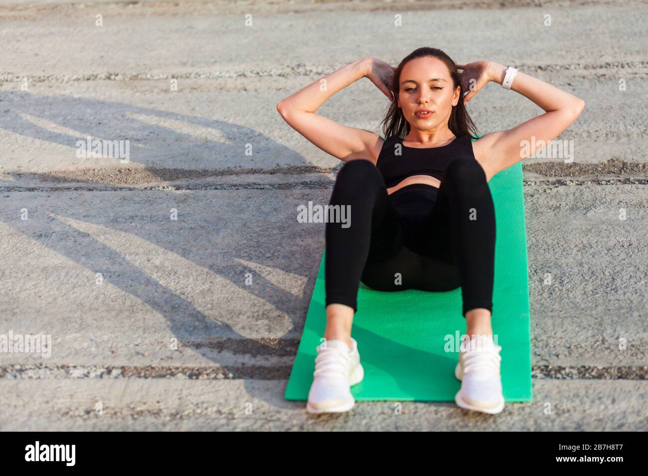 Bonita chica atlética en ropa deportiva ajustada, pantalones negros y top,  acostada en la esterilla haciendo sentadas, ejercicio de crujido,  entrenamiento de músculos abdominales. Atención de salud an Fotografía de  stock -