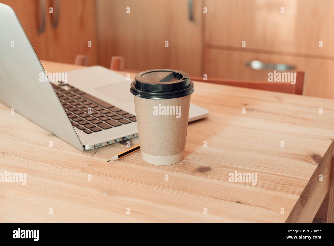 Cappuchino en una taza de cartón de papel en un escritorio con ordenador portátil. Café para llevar Foto de stock