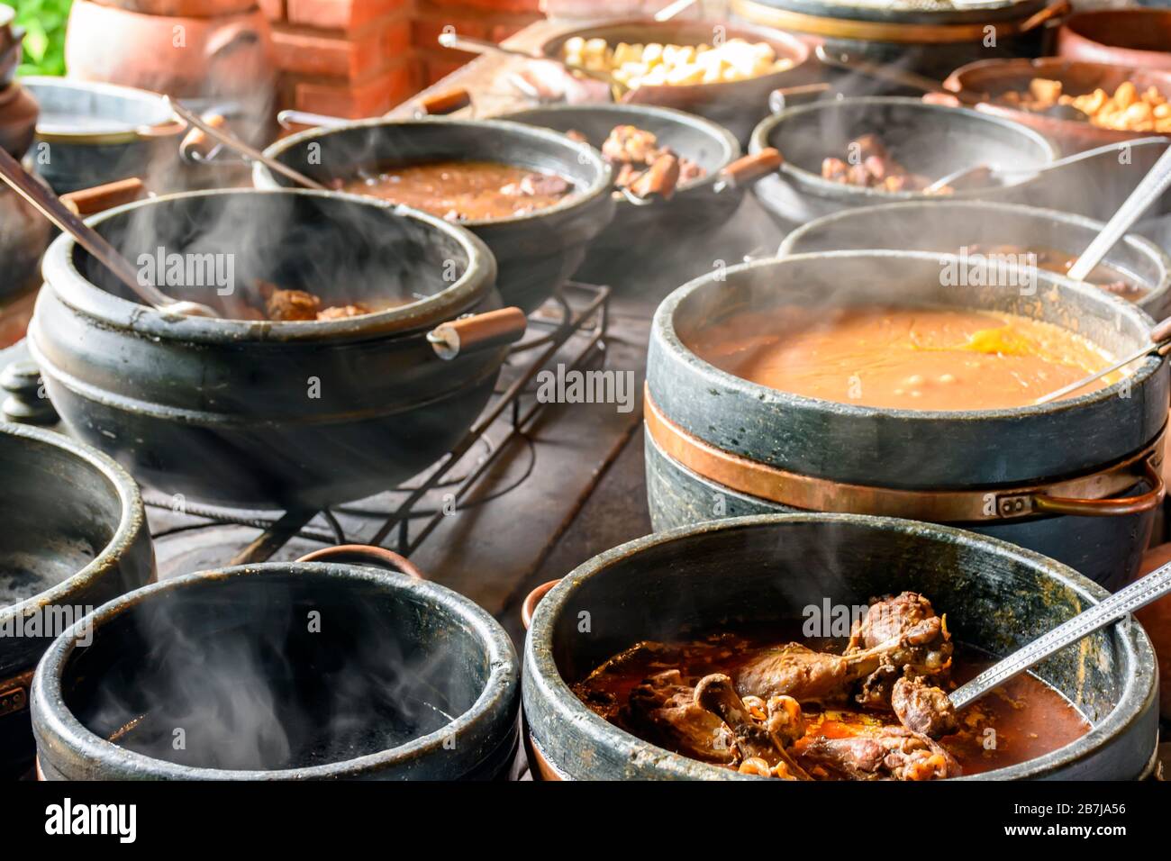Alimentos típicos brasileños colocados en ollas de arcilla y en un plato de metal de una cocina tradicional de madera Foto de stock
