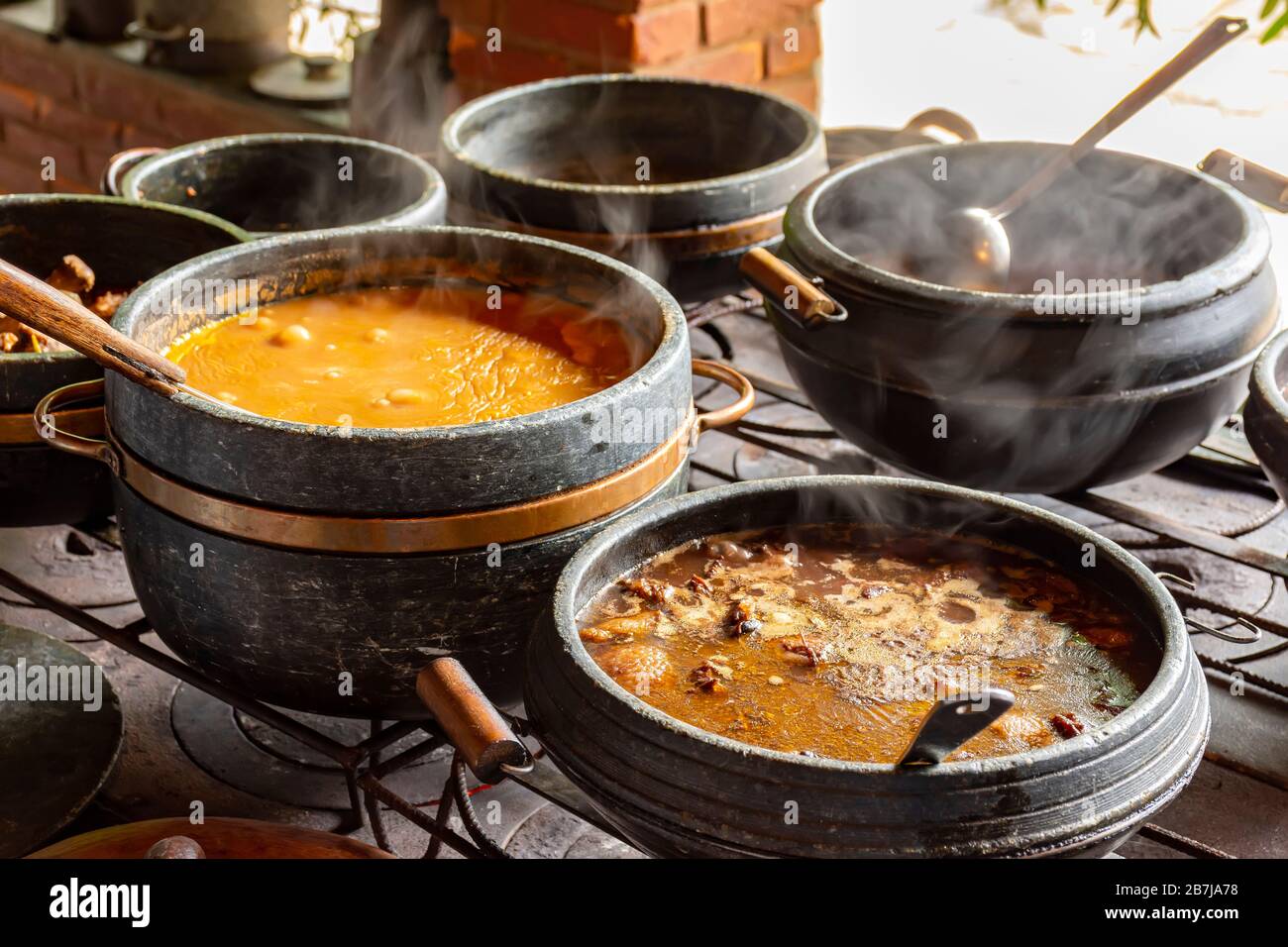 Alimentos típicos brasileños colocados en ollas de arcilla y en un plato de metal de una cocina tradicional de madera Foto de stock