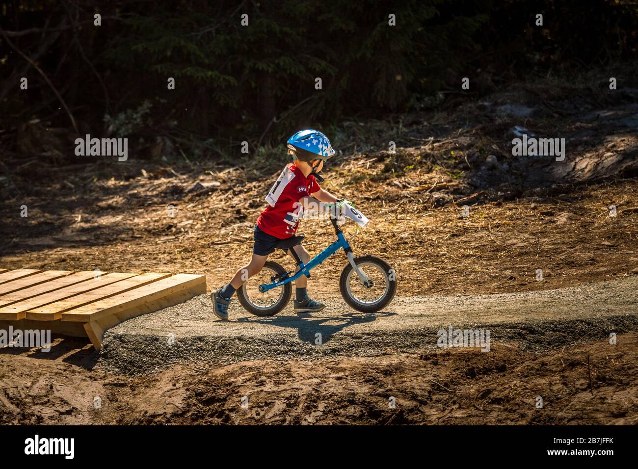niño de 2-3 años en kick-bike, con gafas de sol y casco, en un parque de bicicletas pista de bombas Foto de stock