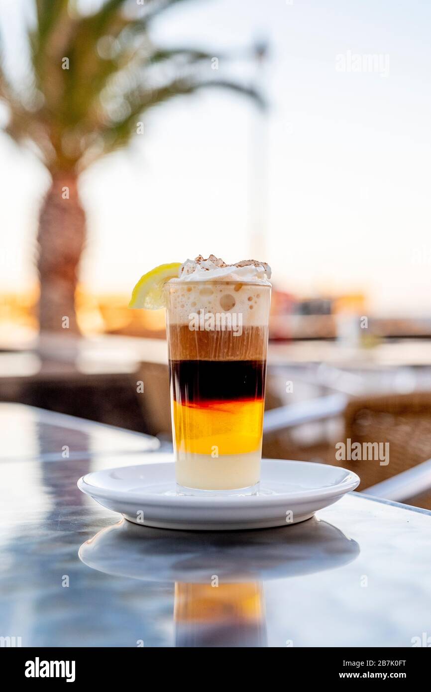 Café combinado con leche condensada de whisky crema de canela y limón en  una taza de cristal en una terraza con una palmera en el fondo Fotografía  de stock - Alamy
