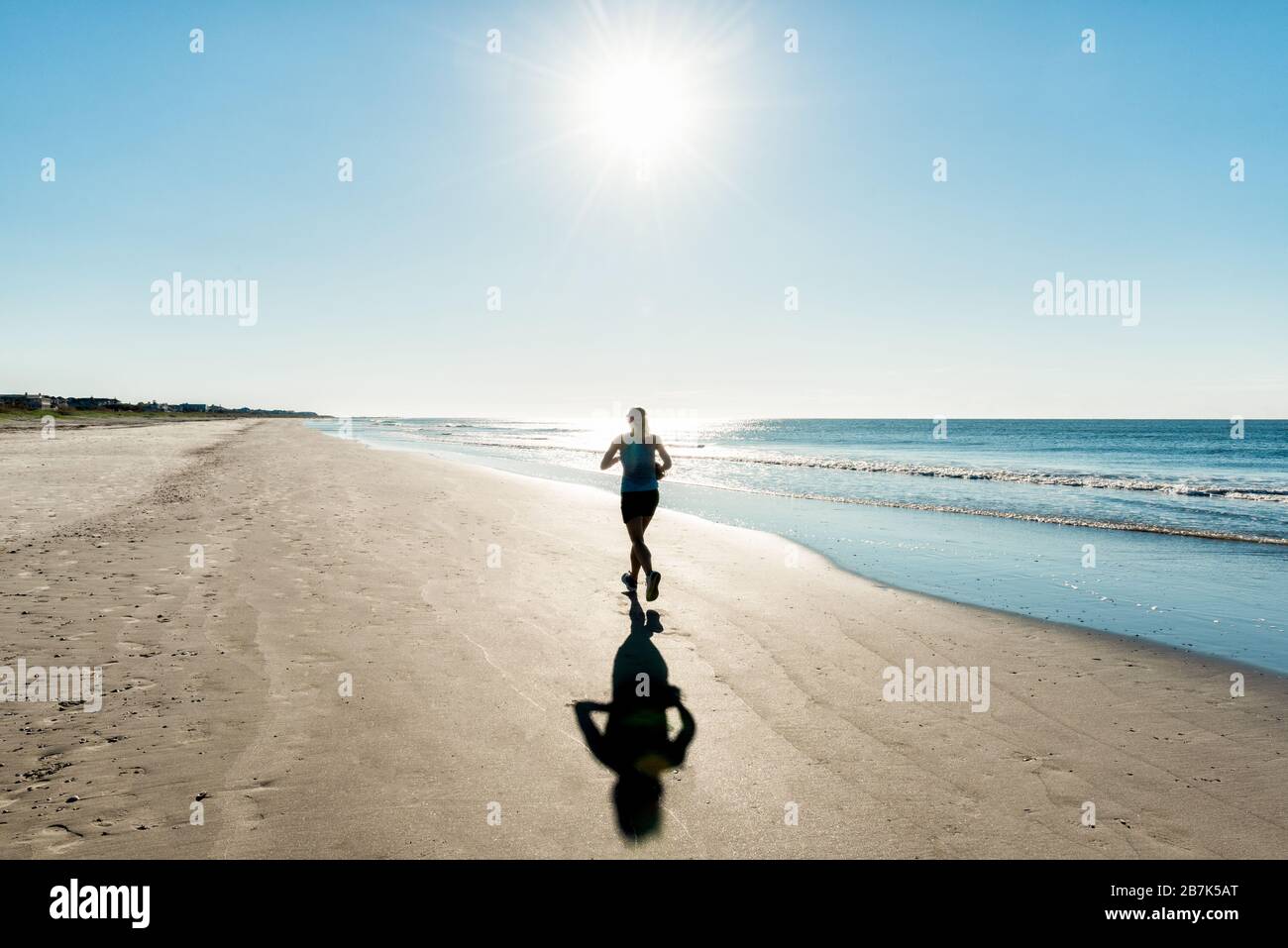 Una mujer disfruta de un paseo temprano por la mañana a lo largo de la costa, mientras el sol sale sobre el Océano Atlántico. Foto de stock