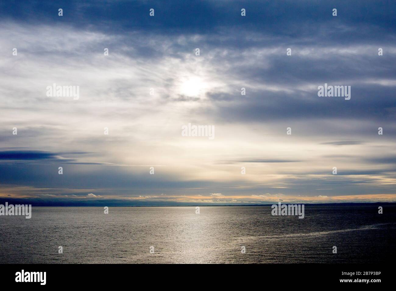 Un gran paisaje de esquí roto sobre un mar tranquilo, el sol rompiendo y arrojando un sutil reflejo sobre la superficie del agua. Foto de stock