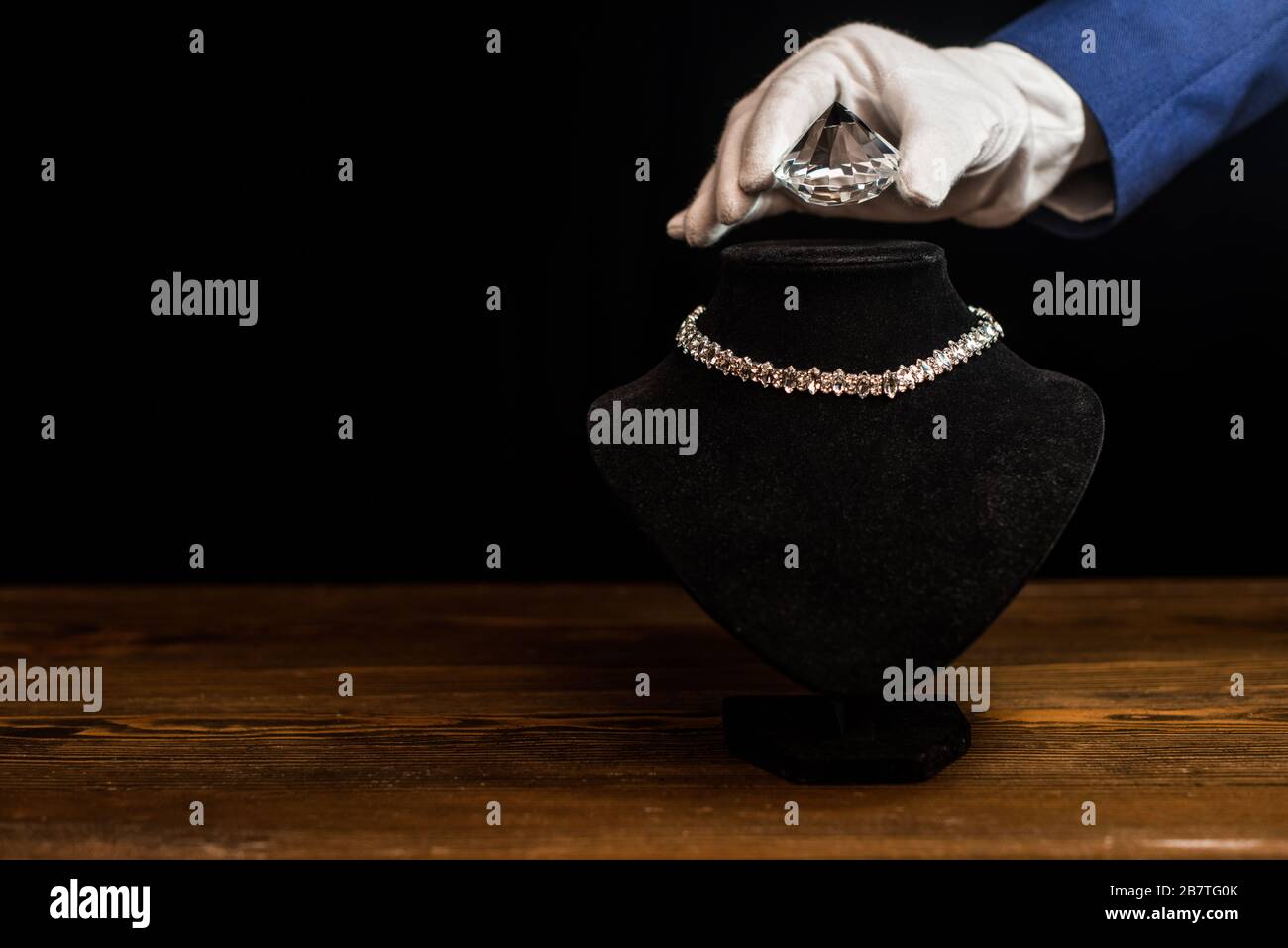 Vista recortada de joyería taser sosteniendo el diamante cerca del collar  en el puesto del collar en la mesa de madera aislada en negro Fotografía de  stock - Alamy