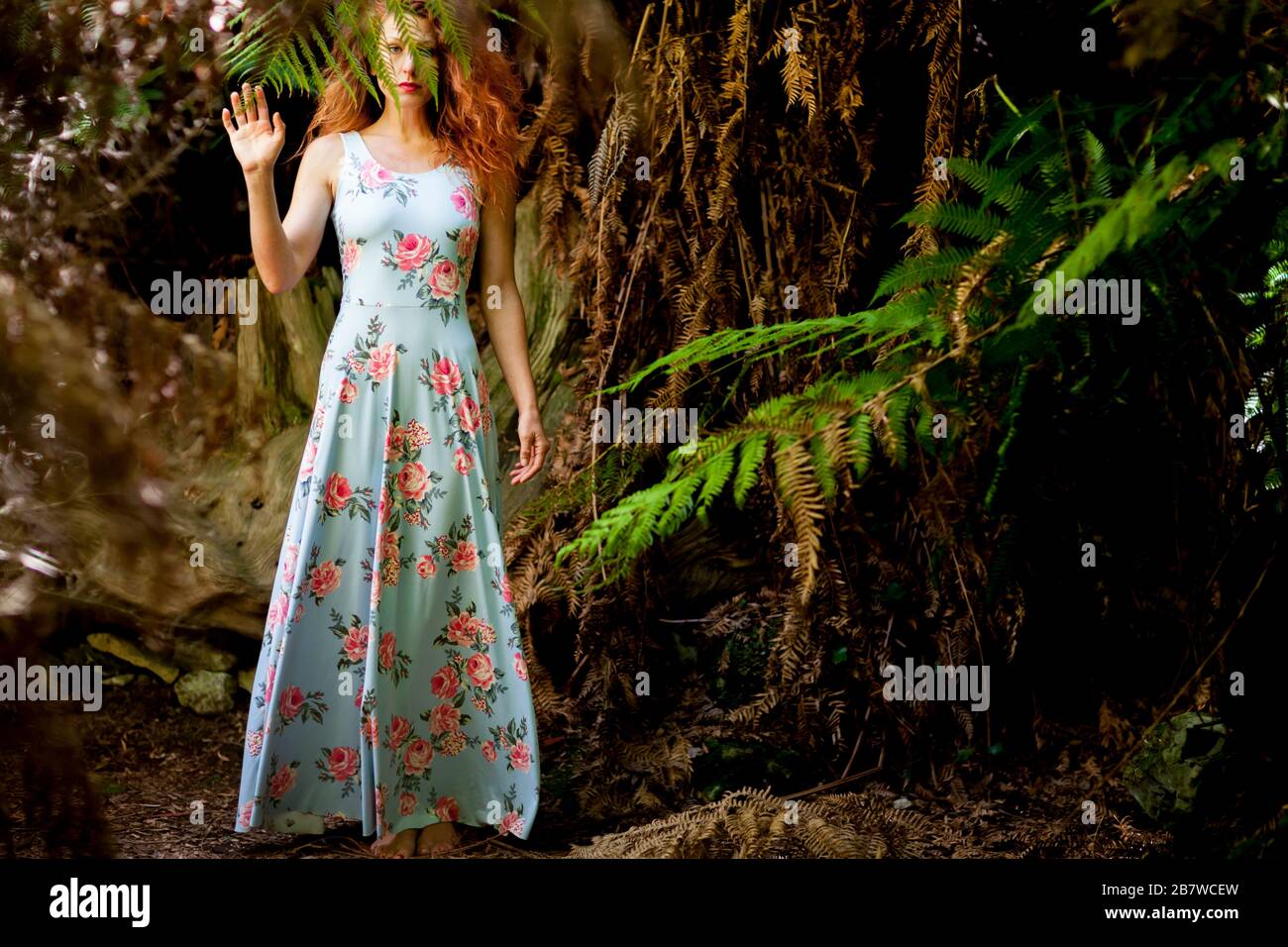 Mujer en vestido floral de pie por Fern Tree en el bosque Foto de stock