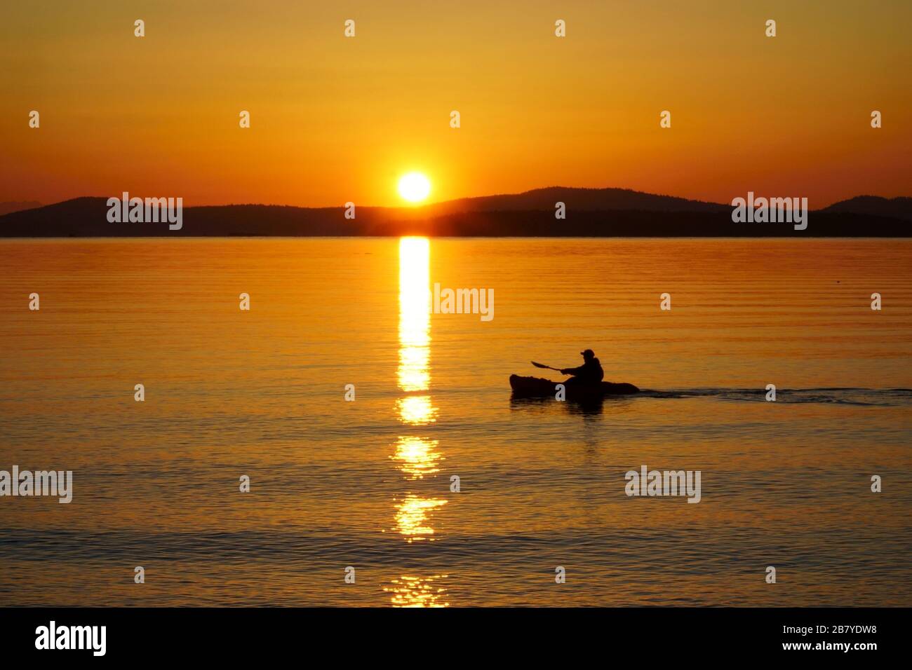 Amanecer en el estrecho de Haro mientras un remo impulsa su kayak a través del sol. Foto de stock