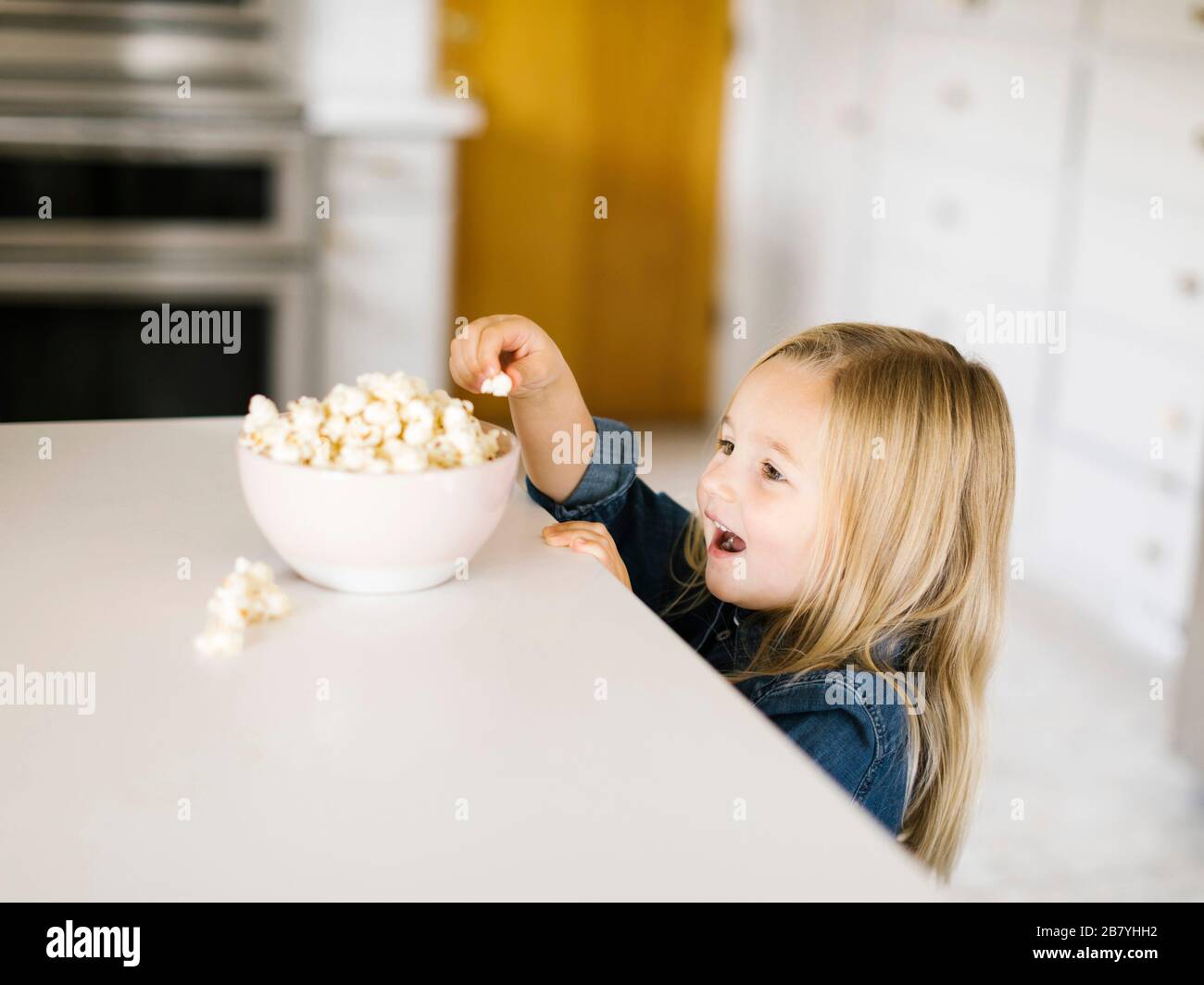 Chica tomando palomitas de maíz de un cuenco en el mostrador de la cocina Foto de stock