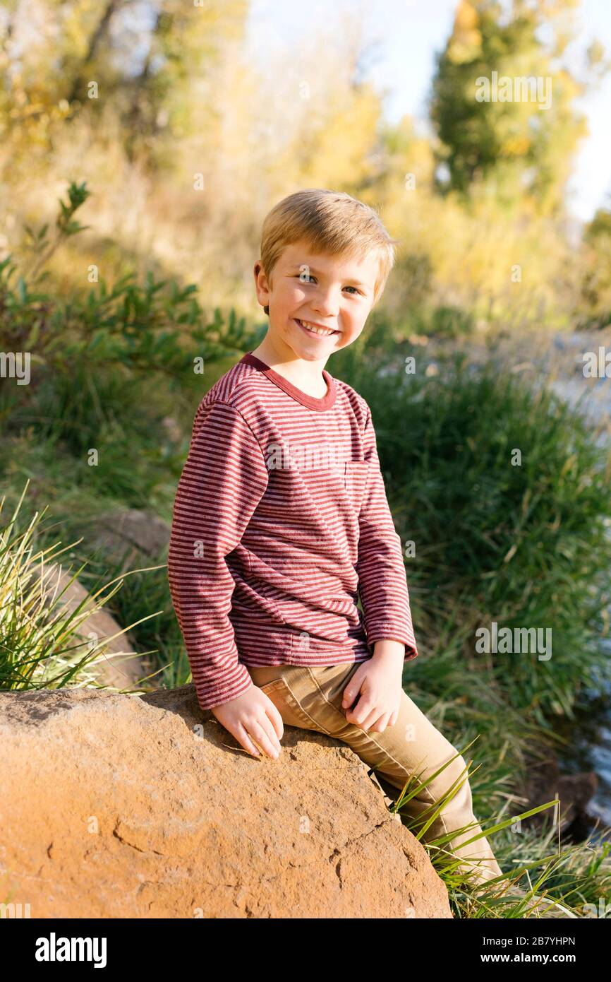 Niño sonriente sentado en el rock Foto de stock