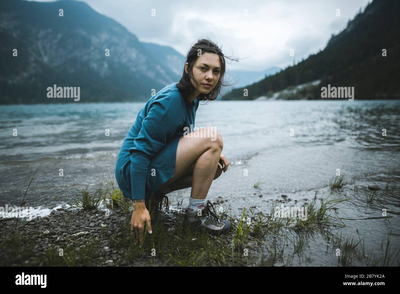 Mujer joven en cuclillas por el lago Foto de stock