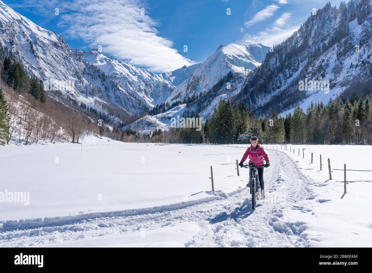 Mujer mayor agradable montando su bicicleta de montaña eléctrica en un soleado día de invierno en los alpes de Allgau cerca de Oberstdorf, Baviera, Alemania Foto de stock