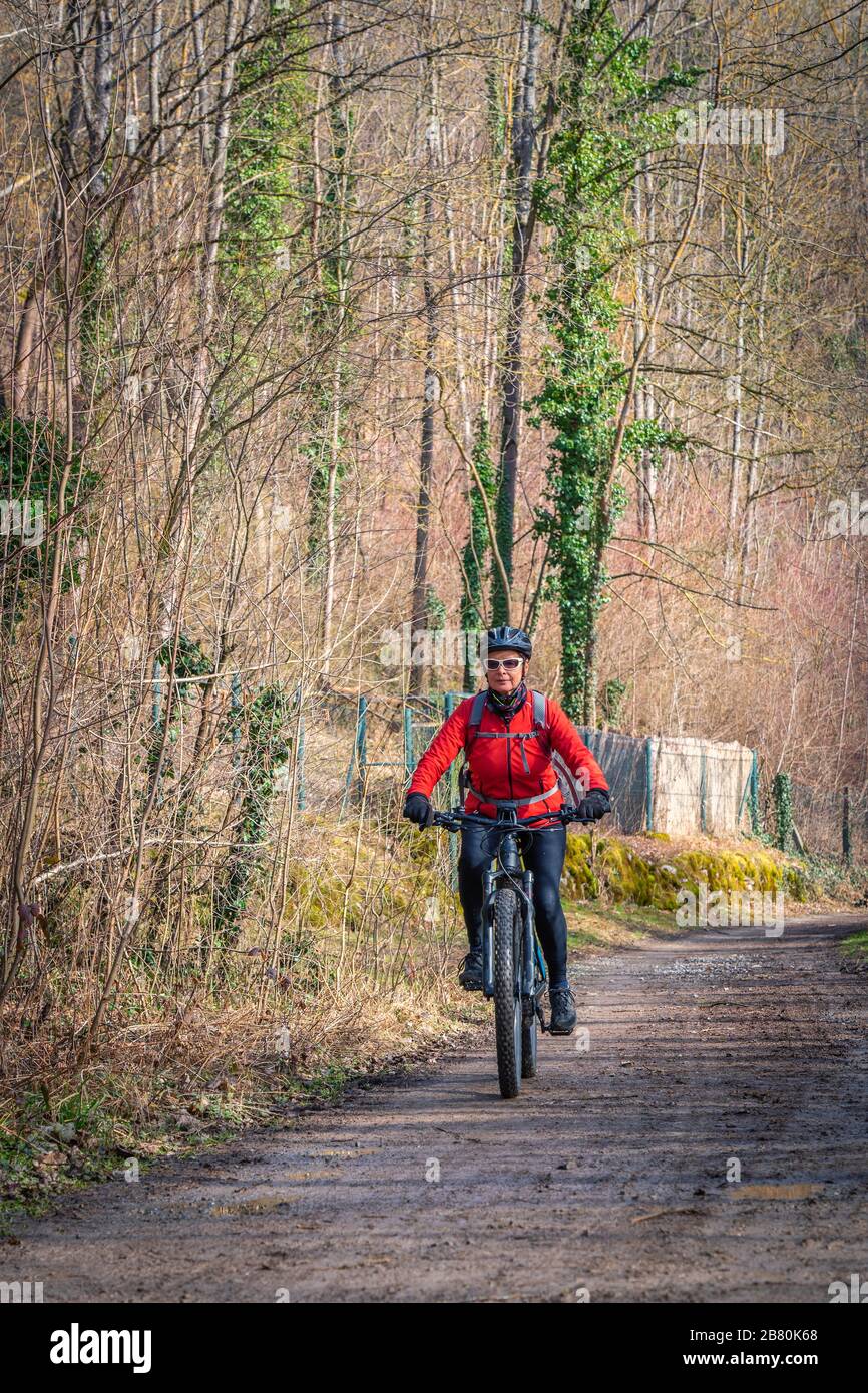Buena mujer de edad activa montando su bicicleta eléctrica de montaña a principios de la primavera a lo largo de un pequeño río cerca de Stuttgart Foto de stock