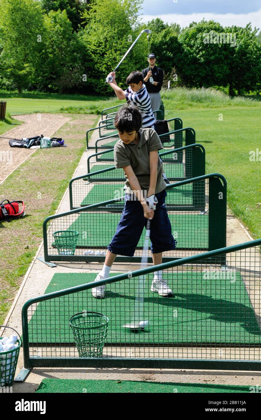 Tres jugadores de golf en acción en el campo de prácticas. Dos niños pequeños y un adulto probando sus habilidades en el Lindfield Golf Club, West Sussex, Inglaterra. Foto de stock
