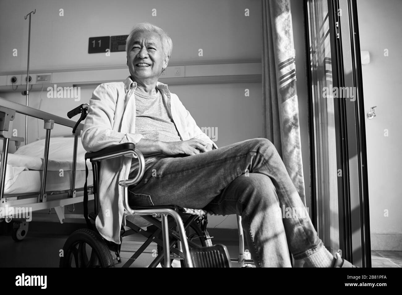 feliz y contento viejo asiático sentado en silla de ruedas en el asilo de ancianos o en el pabellón del hospital, en blanco y negro Foto de stock