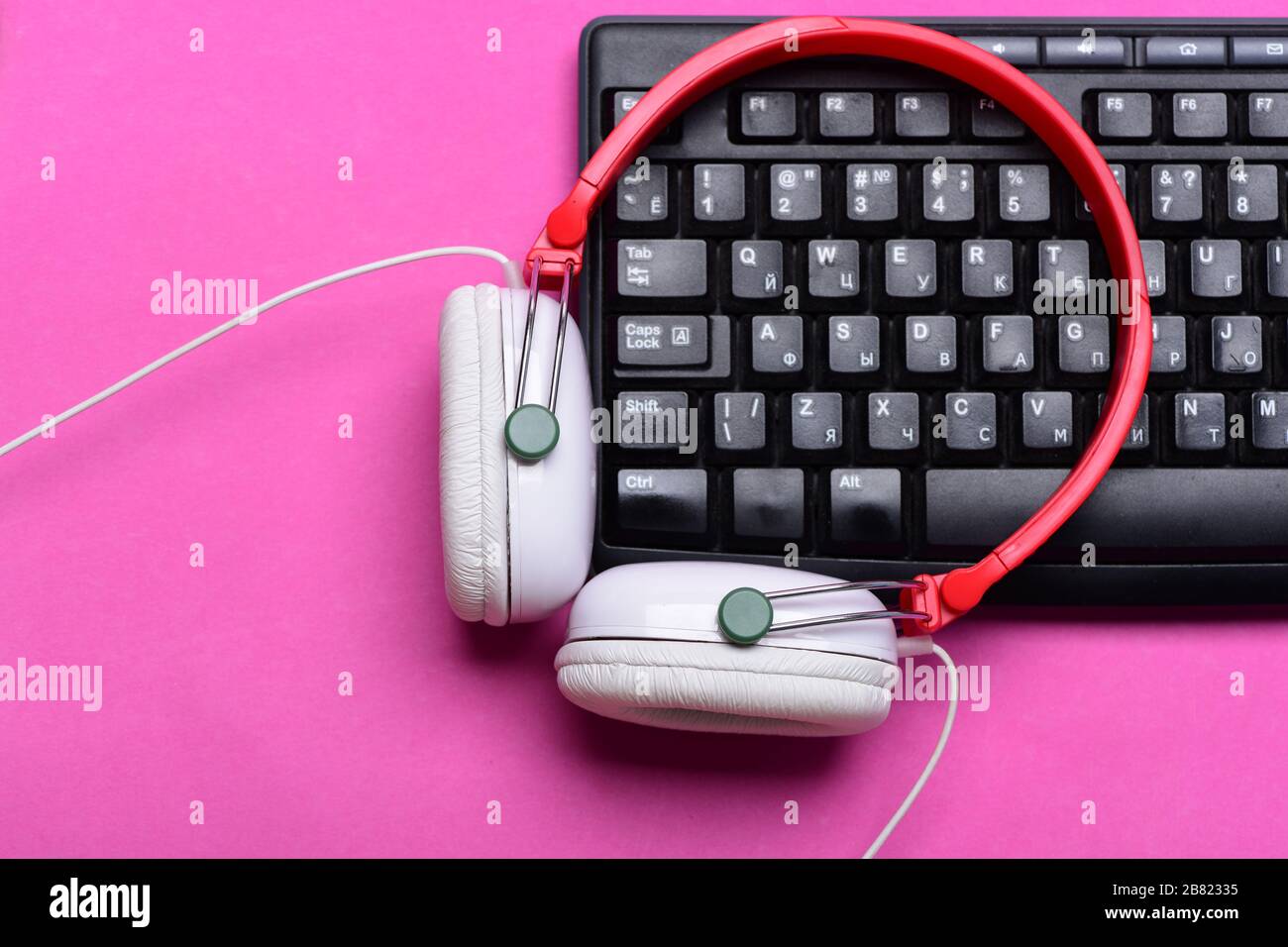 Aparatos electrónicos sobre fondo rosa. Auriculares en colores rojo y  blanco con teclado de ordenador. Grabación de sonido y tecnología. Concepto  de música y equipamiento digital. Auriculares y teclado negro Fotografía de