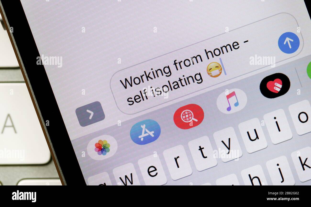Trabajando desde casa, mensaje de texto autoaislado con una máscara de cara emoji, durante el brote de Coronavirus en el Reino Unido Foto de stock