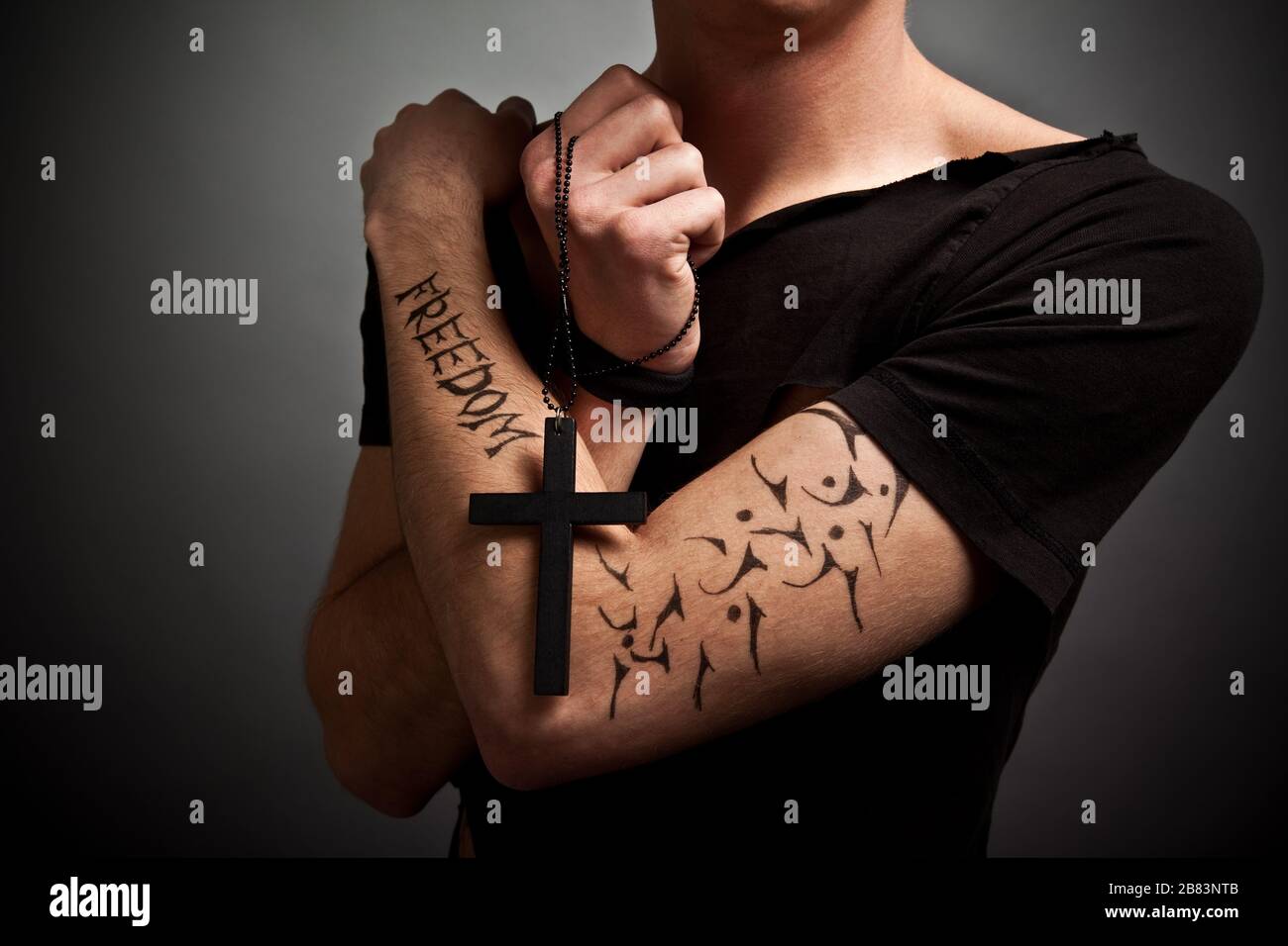 Hombre joven con ropa negra moderna y tatuaje de libertad sosteniendo una  gran cruz negra en las manos con los ojos cerrados. Concepto de estilo de  vida de belleza y moda Fotografía