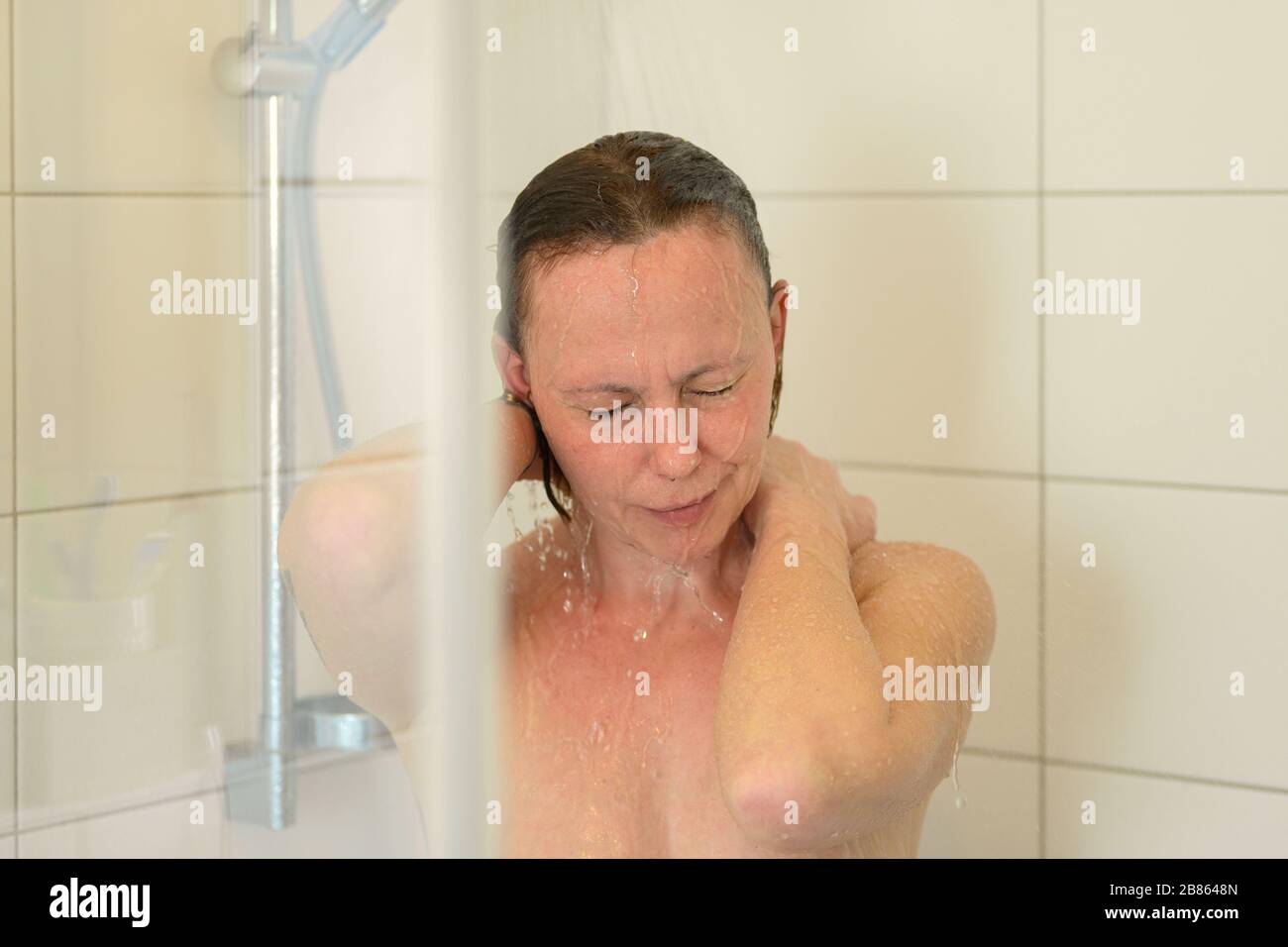 Mujer disfrutando de una ducha caliente enjuagando su cabello después de shampooing bajo el agua corriente en primer plano en un concepto de higiene personal Foto de stock