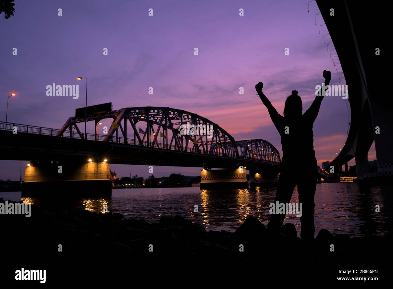 El concepto es exitoso, retroiluminado foto de una mujer sosteniendo un puño para mostrar su deleite, el fondo es un río grande con un puente que cruza sobre th Foto de stock