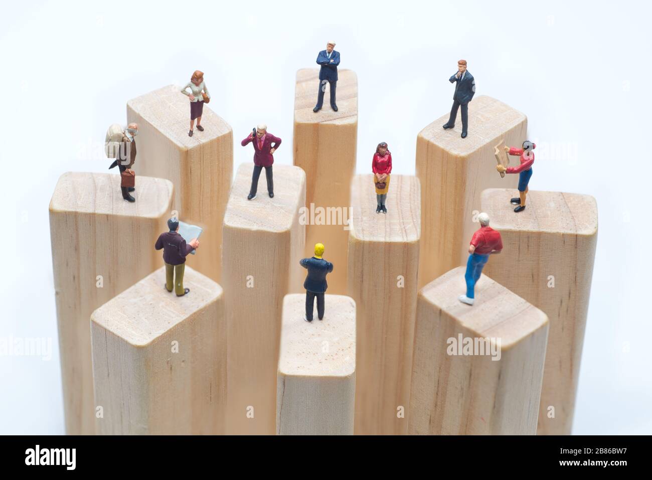Juguetes en miniatura de pie sobre bloque de madera - concepto de distanciamiento social, antisocial o de trabajo en equipo. Foto de stock