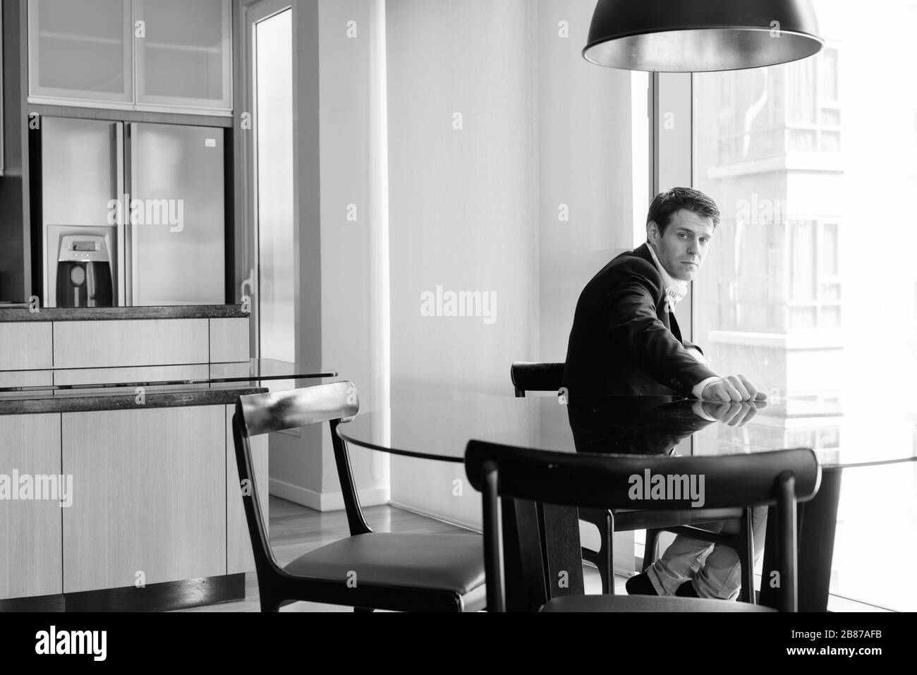 Joven hombre de negocios guapo sentado en el comedor cerca de la cocina Foto de stock
