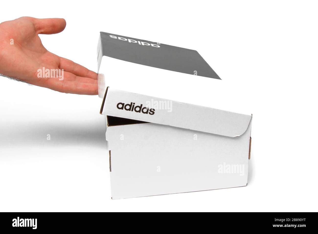 Primer plano mans apertura mano caja en blanco y negro con logo Adidas. La  caja de zapatos está aislada sobre un fondo blanco. San Francisco, EE.UU.,  marzo de 2020 Fotografía de stock -