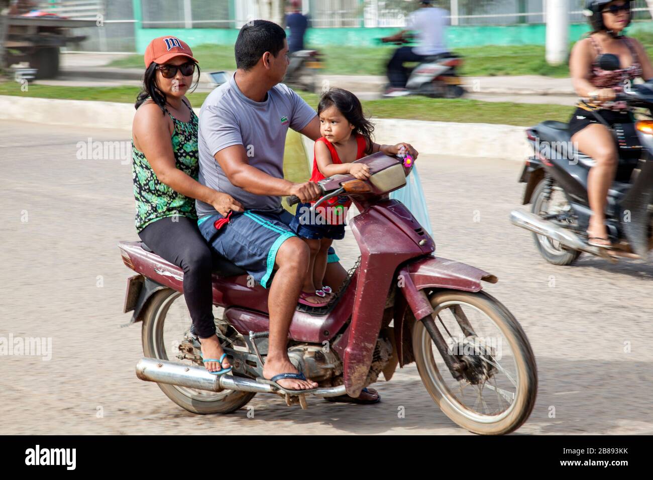 Tres arriba, mamá, papá y niño en una moto que conduce sin cascos, en Leticia, Amazon, Colombia, América del Sur. Foto de stock