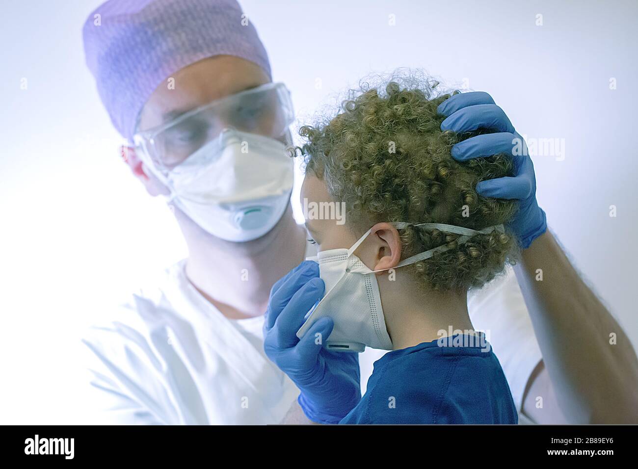Un trabajador médico está ayudando a un niño de 4 años a usar la máscara del coronavirus para protegerlo de la infección, en la zona roja de la epidemia en la ciudad de Foto de stock