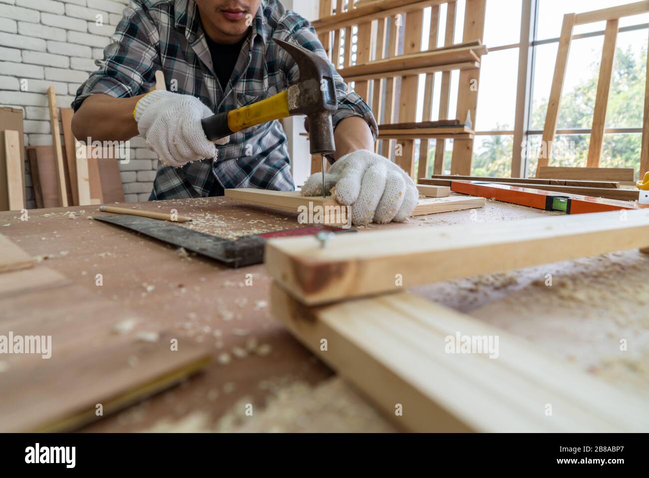 Carpintero trabajando en artesanía de madera en el taller para producir material de construcción o muebles de madera. El joven carpintero asiático utiliza herramientas profesionales para Foto de stock