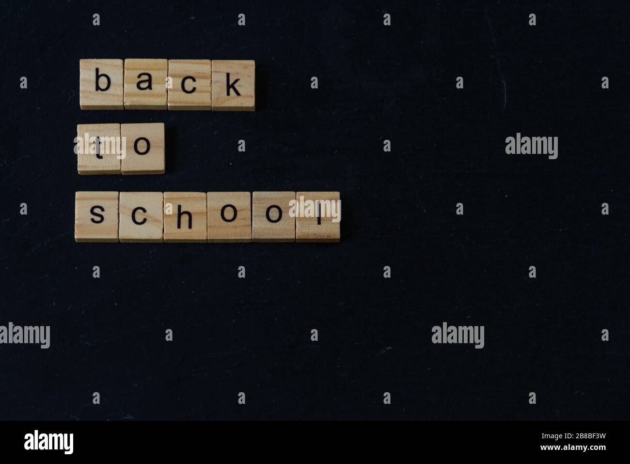 Volver a la Escuela escrito en bloques de madera de letras sobre fondo oscuro pizarra. CopySpace a la derecha y abajo. Foto de stock