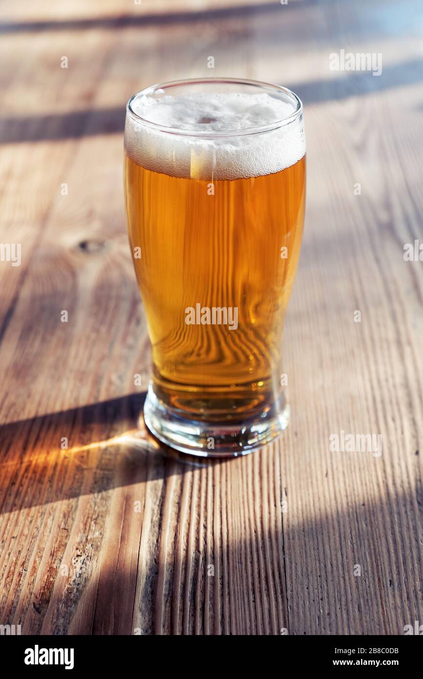 Copa de cerveza fría en la mesa de madera de un pub bajo la luz natural de la tarde Foto de stock
