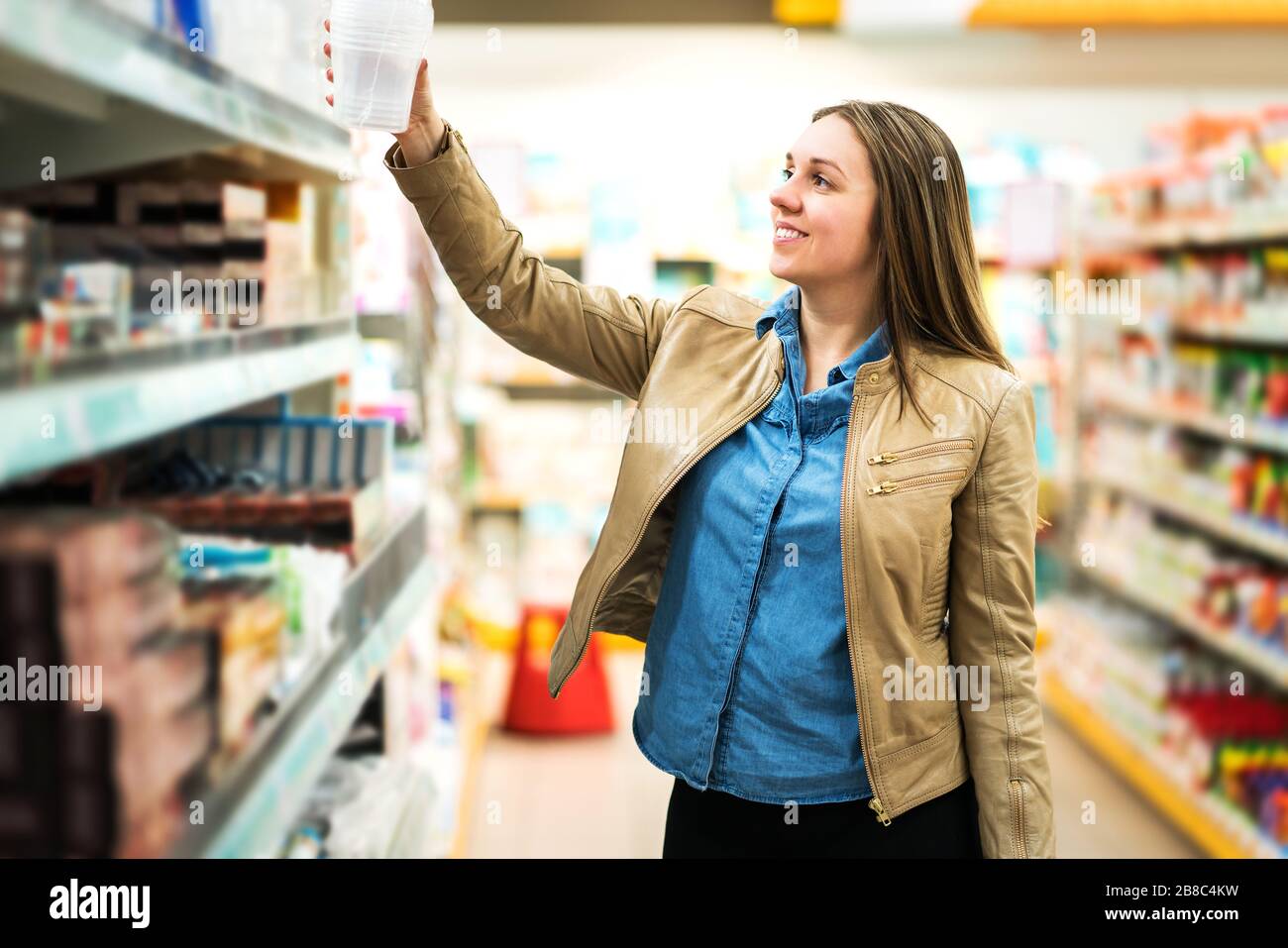 Cliente femenino con paquete o artículo en el supermercado. Mujer tomando el producto de la estantería en la tienda de comestibles. Concepto de venta al por menor, venta y consumismo. Foto de stock