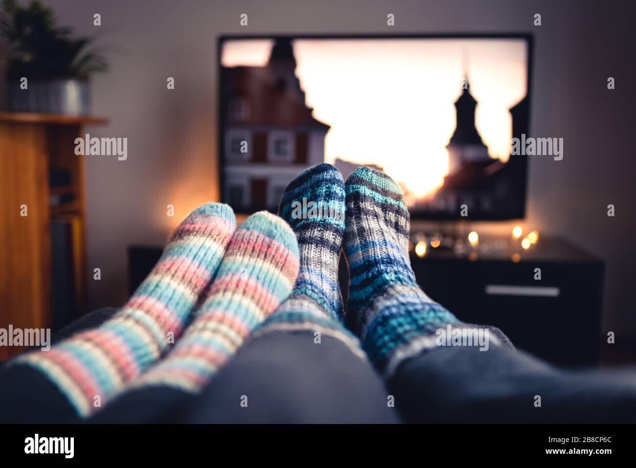 Pareja con calcetines y medias de lana viendo películas o series en la televisión en invierno. Mujer y hombre sentados o acostados juntos en el sofá-cama en casa. Foto de stock